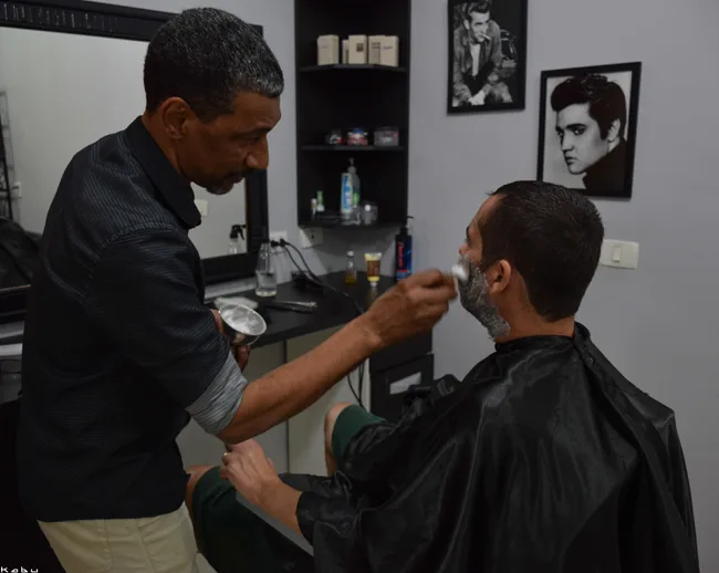 Barbeiro fazendo a barba de um cliente sentado